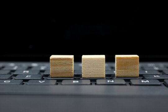 Three wooden blocks arranged on a computer keyboard with a dark blurred background, creating copy space for text and various creative, business, technology, and educational concepts.