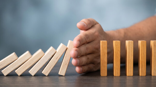 Hand stopping dominoes from falling, symbolizing intervention, risk management, and protection against chain reactions.