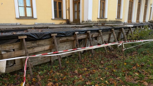 The foundation of an old building, cordoned off with warning tape, featuring wooden supports and black film for renovation work.