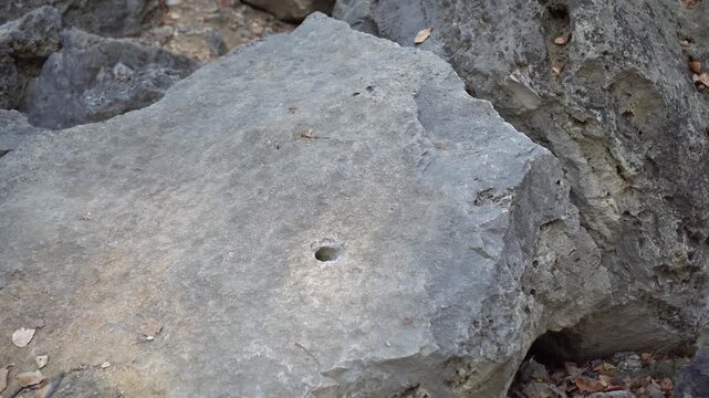 Wide view of a drilled hole in a rocky mining site, prepared for dynamite placement during ore extraction amid a rugged geological landscape.