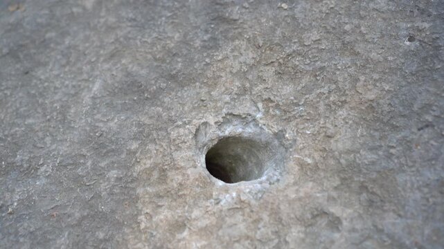 A moving close up of a drilled hole in solid rock prepared for dynamite placement during ore mining, revealing rough textures and geological details.