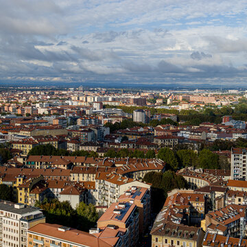 Turin's urban neighborhoods and red tiled rooftops stretching beneath a cloudy sky