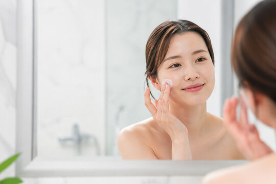 鏡を見ながら頬にクリームを塗る日本人女性