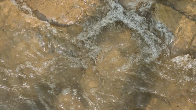 Top down slow motion of clear mountain stream water rippling over golden brown riverbed rocks