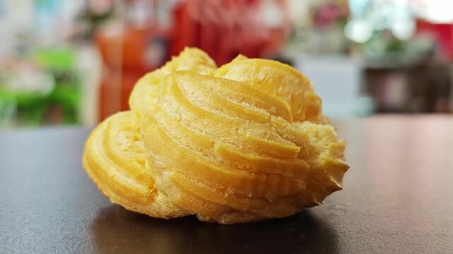 Delicious golden choux cream pastry sitting on a dark surface with colorful bokeh background.