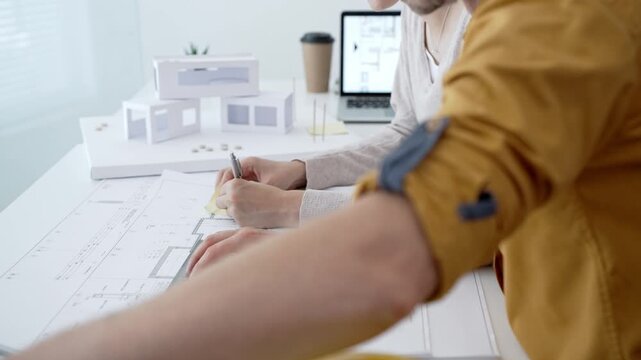 Architects collaborating on building blueprints, discussing design details and making notes with a ruler and pen, working on a new project in a modern office