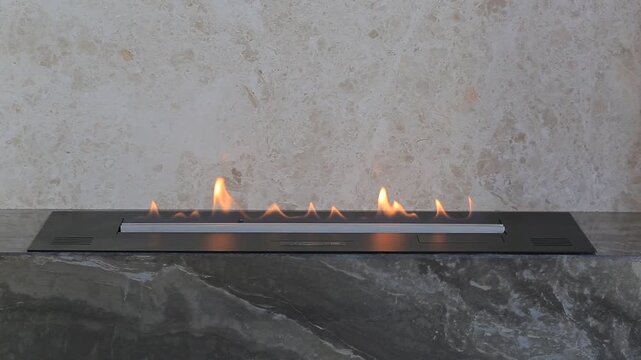 Cinematic focus pull of linear bioethanol fireplace built into dark marble portal changing from sharp burning flames to warm orange blurred bokeh circles