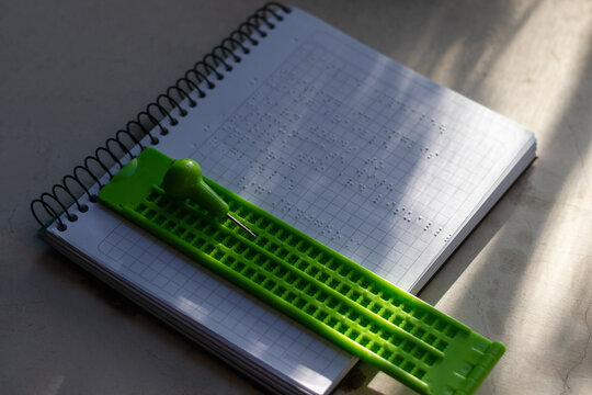 Vertical stock photo of green braille writing slate and stylus on embossed Braille spiral notebook