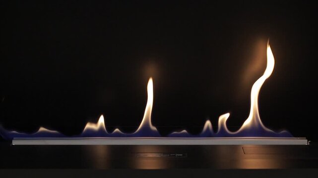Close up automatic long burner eco fireplace changing from sharp blue and yellow flames to warm orange blurred bokeh circles against dark background