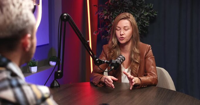 Confident woman expert or narrator telling personal story into studio microphone responding to male interviewer questions engaged in guided on air conversation during podcast or live streaming session