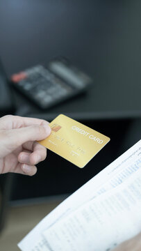 Close up of a hand holding and slowly rotating a gold credit card while reviewing bills and invoices, representing credit card debt, financial decisions, bill payment and personal finance management