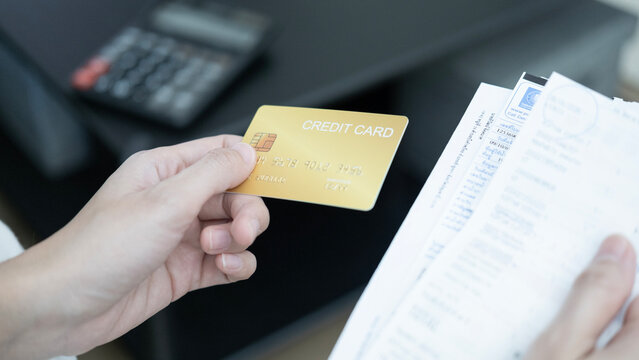 Close up of a hand holding and slowly rotating a gold credit card while reviewing bills and invoices, representing credit card debt, financial decisions, bill payment and personal finance management.