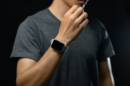 Man Wearing a Smart Watch on Wrist in Casual Grey T-Shirt with Dark Background