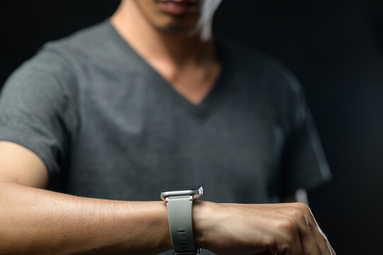 Young Man Checking Smartwatch on Wrist, Casual Clothing, Dark Background