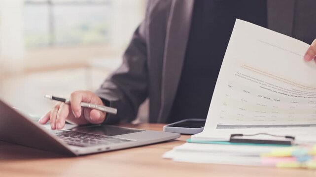 Businessman reviews financial documents enters data on laptop at office desk. Corporate accounting audit, tax invoice calculation, financial reporting analysis, contract management review.
