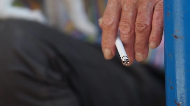 Close view of a person holding a cigarette beside a blue chair