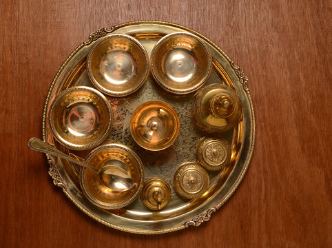 A vintage Pooja thali made of brass metal. A top view of a handcrafted ornamental plate with many containers placed in it. View from above. Indian traditional utensils and servewares.