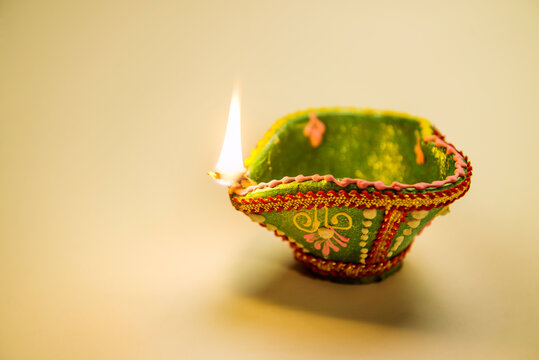 Close up of an illuminated, decorative Diwali lamp placed on a plain background. Diwali objects and background.