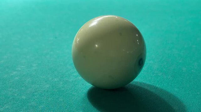 Wooden cue stick tip strikes white Russian billiard ball closely on green felt table cloth. Tracking layout, precision strategy game training process and active leisure hobby competition.