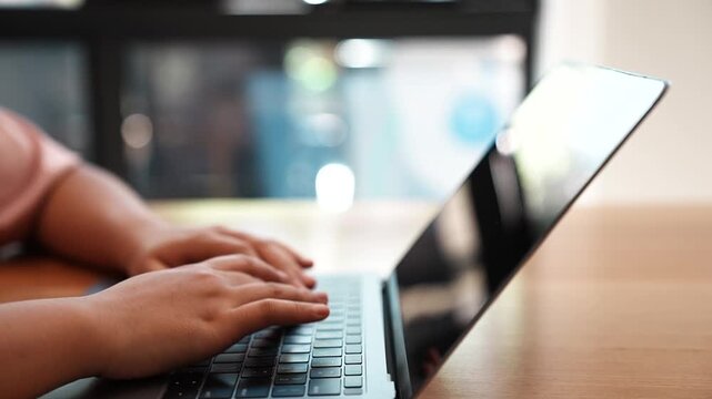 Close up footage of a person typing on a laptop keyboard at a wooden table indoors, representing digital technology, online communication, remote work and everyday computer use.