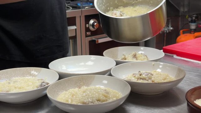 Chef plating creamy risotto and adding grated cheese in restaurant kitchen