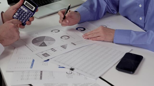 brainstorming, discussing reviewing financial dashboard. Colleagues reviewing financial dashboard reports, comparing charts and discussing figures with calculator and laptop at office table
