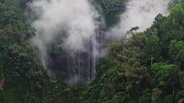 Telephoto Drone Shot Slowly Moving Left to Reveal Tumpak Sewu Waterfall Behind Trees on an Overcast Day in East Java, Indonesia