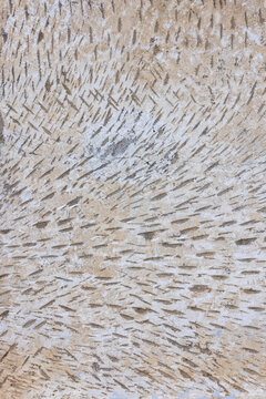 Close-up view of a textured surface featuring light brown and off-white colors. Dark brown indentations create a pattern of parallel marks, improving adhesion of stucco.