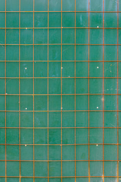 Close-up view of a weathered green surface featuring a grid of orange metal bars. The surface shows visible scratches and fasteners, creating an abstract and textured backdrop.