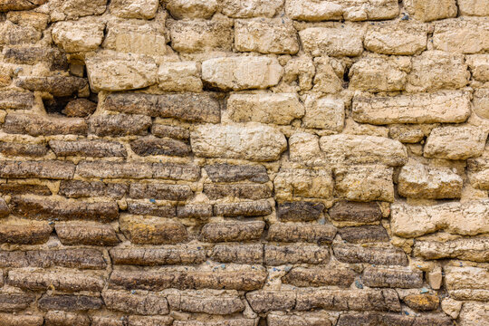 Full-frame close-up view of an aged wall made from sun-dried mud bricks or clay blocks. Surface displays natural textures, imperfections, and a sense of history.