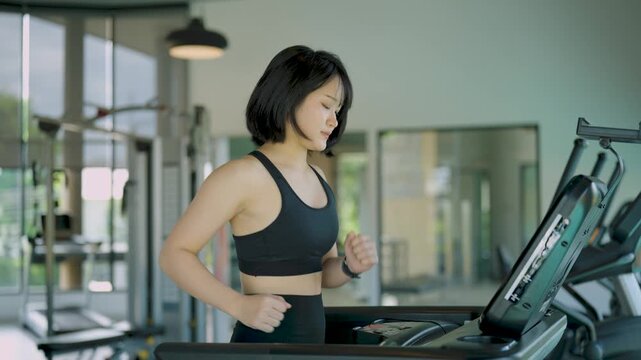 Young woman in black sportswear running on treadmill in bright modern gym for fitness training