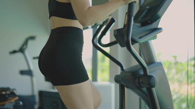 Woman in black shorts exercising on elliptical trainer in bright gym with natural light during workout session