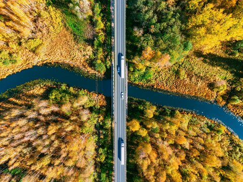 Aerial view of logistics trucks and hybrid electric cars crossing river bridge in autumn