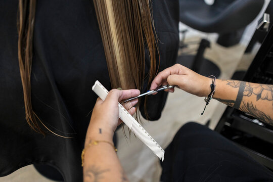 Hairdresser trimming long hair with scissors and comb in salon