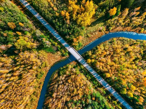 Aerial view of a wooden bridge crossing a winding river amid vibrant autumn foliage