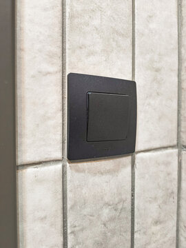 Black wall switch mounted on pale stone tile wall. Minimalist electrical fixture in an architectural detail. Home electricity and interior utility. Modern wall hardware and building surfaces