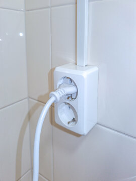 White power cord plugged into a wall socket in tiled interior. Household electricity and electrical connection. Home safety and energy use concept. Utility installation