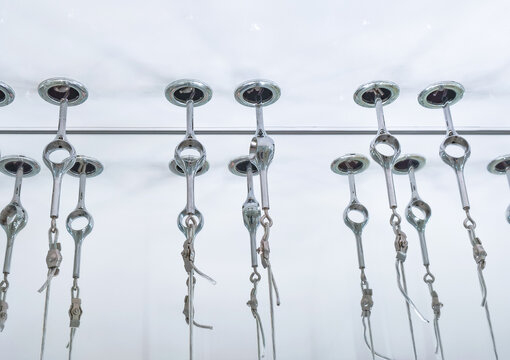 Rows of stainless steel cable fittings suspended from a white ceiling. Industrial rigging hardware and wire rope installation. Mechanical engineering and construction equipment