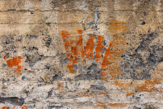 Close-up view of a weathered concrete wall showcasing rough textures and horizontal lines from construction. Patches of orange discoloration and embedded metal elements highlight the wall's natural