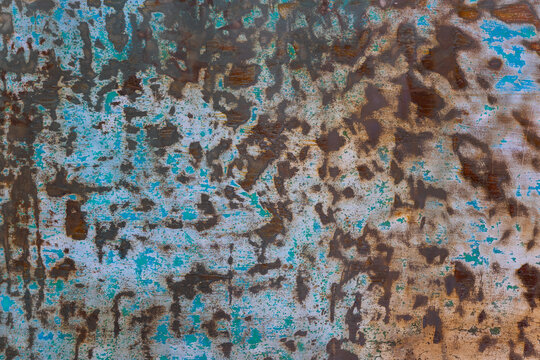 Close-up view of a weathered metal surface featuring peeling blue paint that reveals rust underneath. The rough texture and mottled pattern create an abstract background suitable for various design