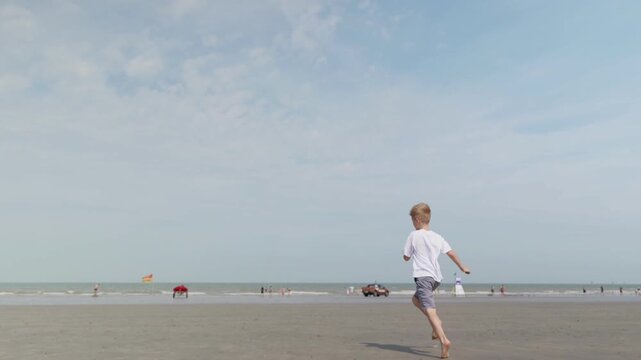 Smiling boy running barefoot across a sandy beach under a blue sky running toward the sea