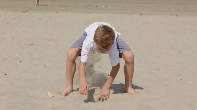 Boy scooping sand with his hands on a sunny beach slow motion a vacation by the sea