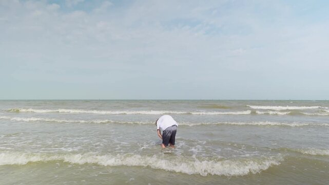 Boy standing in shallow seawater raising arms up slow motion and spinning around