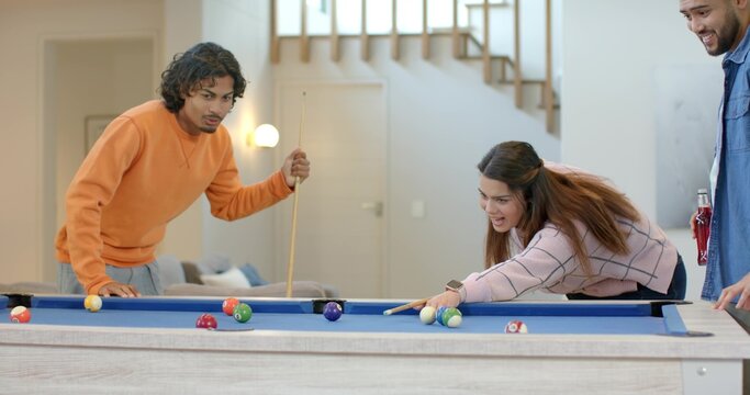 Asian friends playing pool in rec room, woman leaning over blue table aiming amid billiard balls