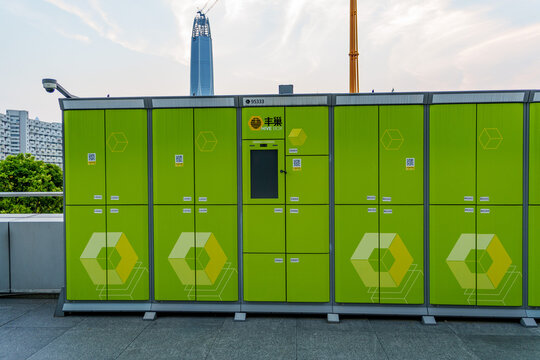 Modern green automated parcel delivery locker station in an urban setting with skyscraper backdrop