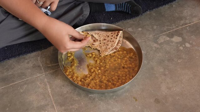 Rural Indian schoolboy eating midday meal of dal and chapati at school, child nutrition, school meal programs, food security, student welfare, and access to nutritious food in rural India. Closeup