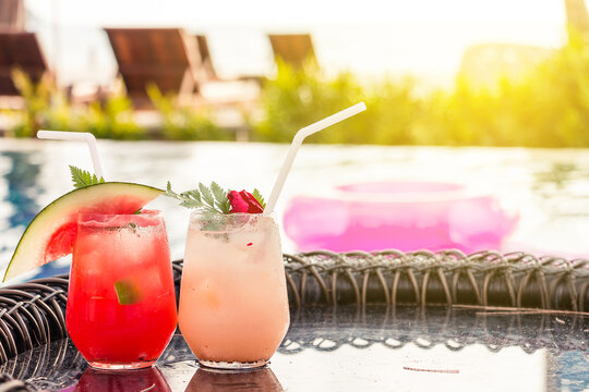 Lychee and Watermelon soda cocktails on table with blurred poolside and beach background. Summer drinks concept.
