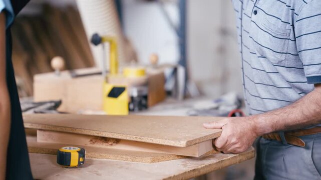 Carpenter's hands holding a wooden plank at his workbench. A professional joiner working with wood and measurement tools in a carpentry shop