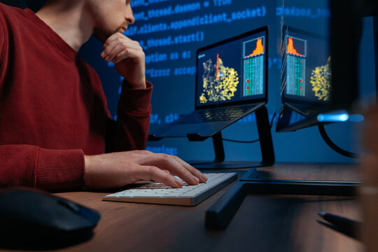 Close-up of a male coder hand on a keyboard in a dark high-tech workspace with monitors, data science graphs and programming code projection background, working on a AI-related task.