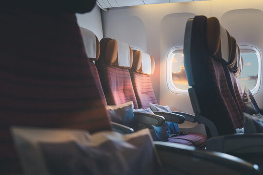 Window plane travel view at sunset or sunrise, empty airplane seats inside airline cabin with morning light, clouds and sky through aircraft windows, business trip, holiday journey  flight background.